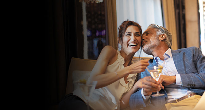 man kissing laughing woman on the cheek holding a martini glass on a new years eve holiday cruise