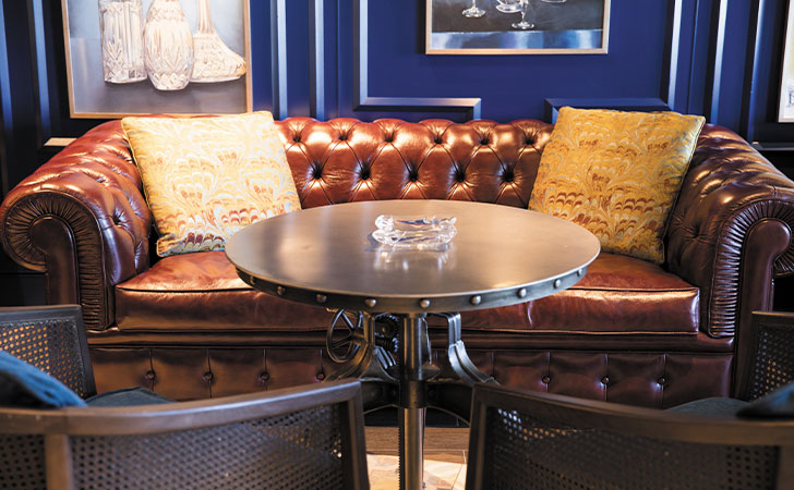 connoisseur club is decorated with a brown leather sofa, blue walls and metal table
